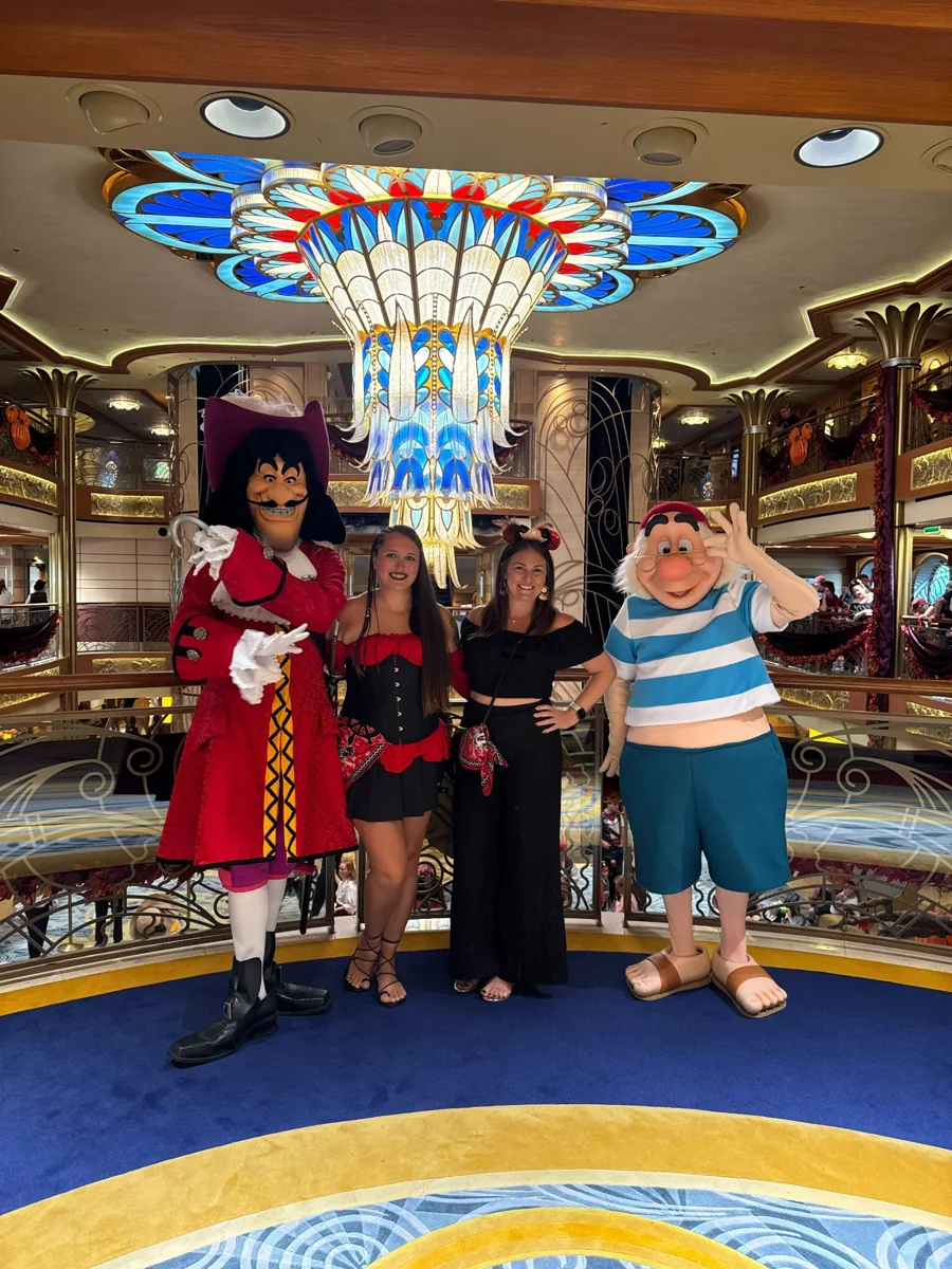 Two advisors with Captain Hook and Mr. Smee in a Disney cruise ship atrium.