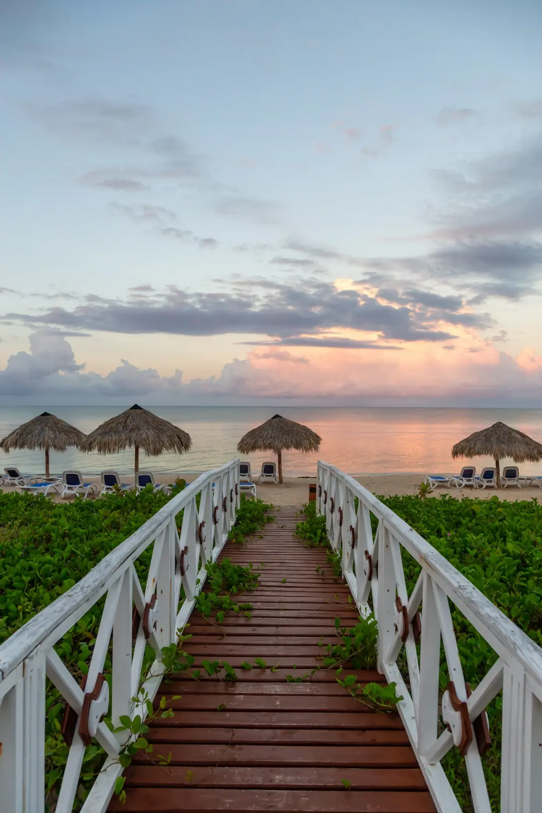 A wooden boardwalk leading toward a quiet beach and the sea at sunset