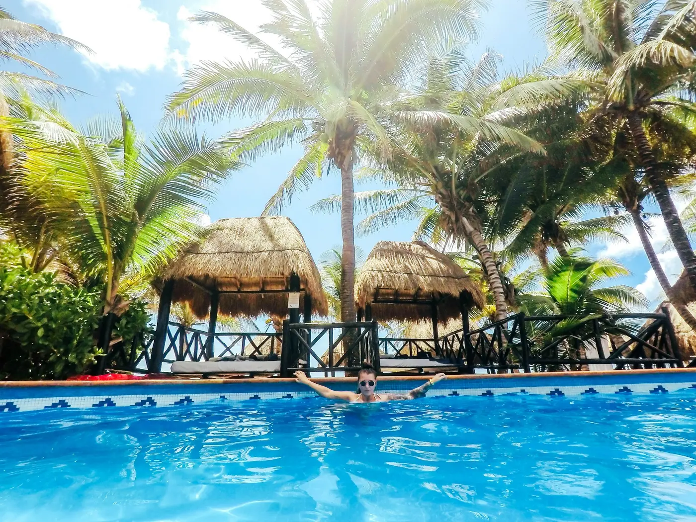 A child swimming in a tropical pool beneath palm trees and thatched pavilions