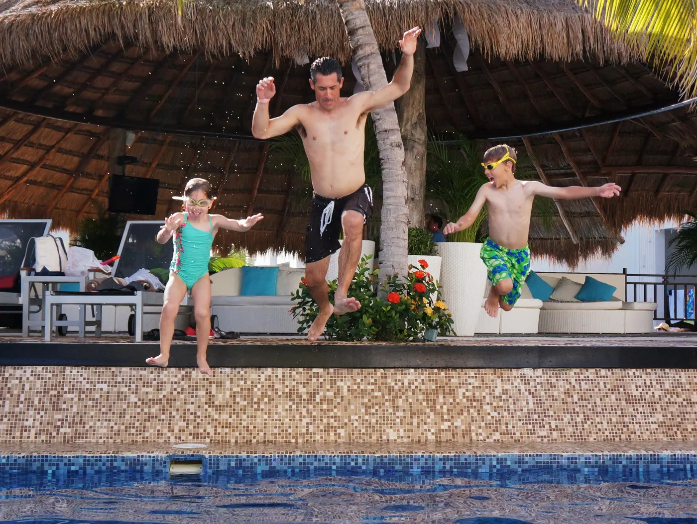 A father and two children jumping into a resort swimming pool together