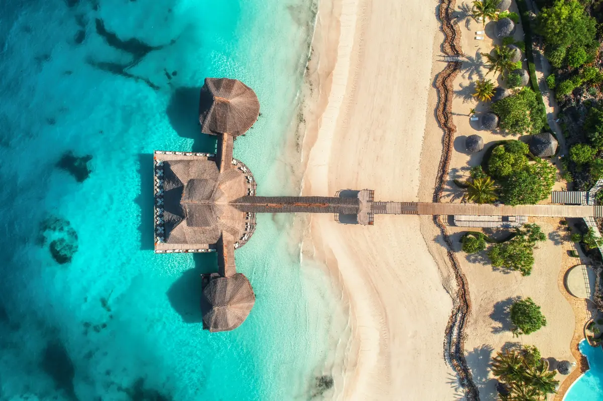 An aerial view of a resort pavilion over turquoise water beside a sandy beach