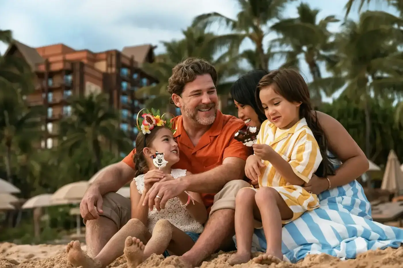A family sharing Mickey-shaped ice cream bars on the beach at Aulani.