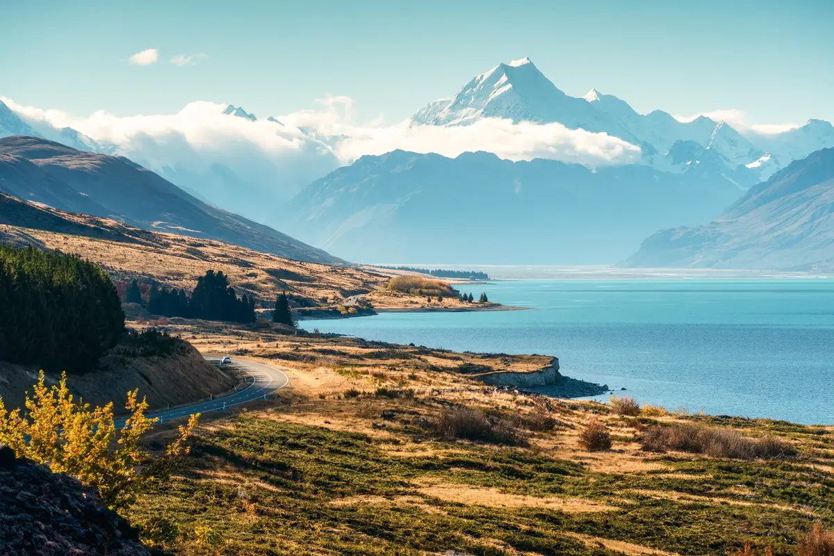 A winding road beside a mountain lake and snowy peaks