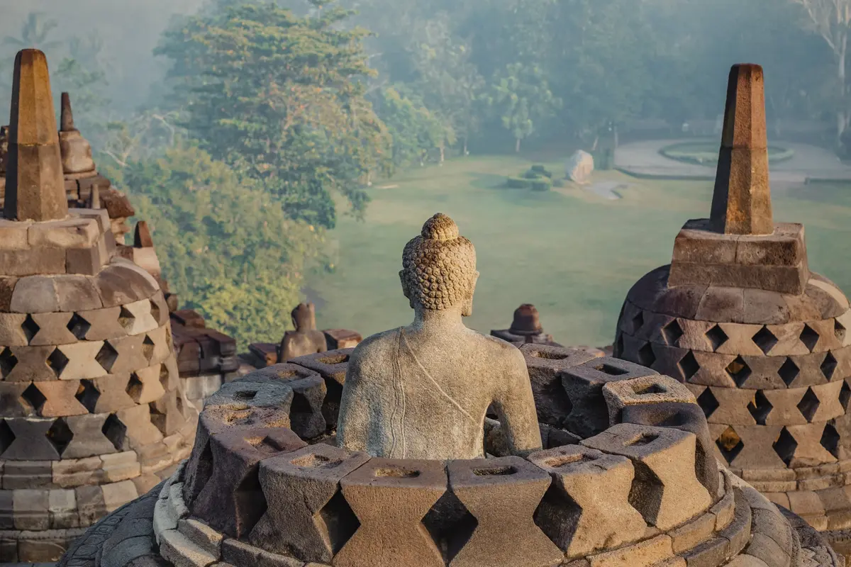 A Buddha statue and stone stupas overlooking a green landscape
