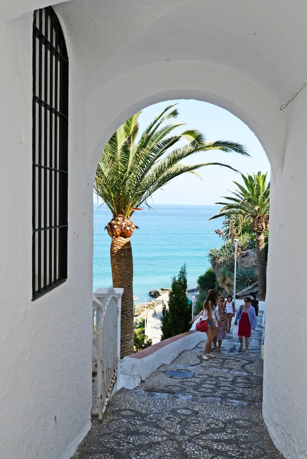 A white archway opening onto a palm lined path toward the sea