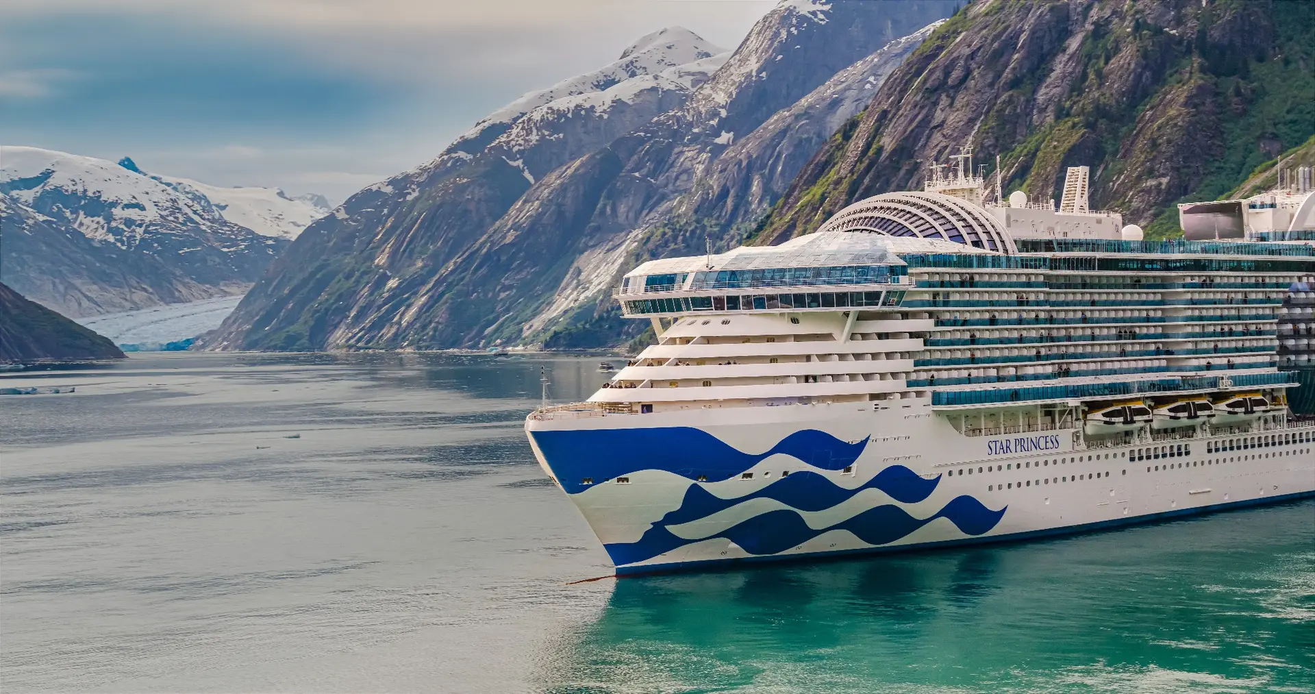 A Princess cruise ship beside steep mountains in Alaska.