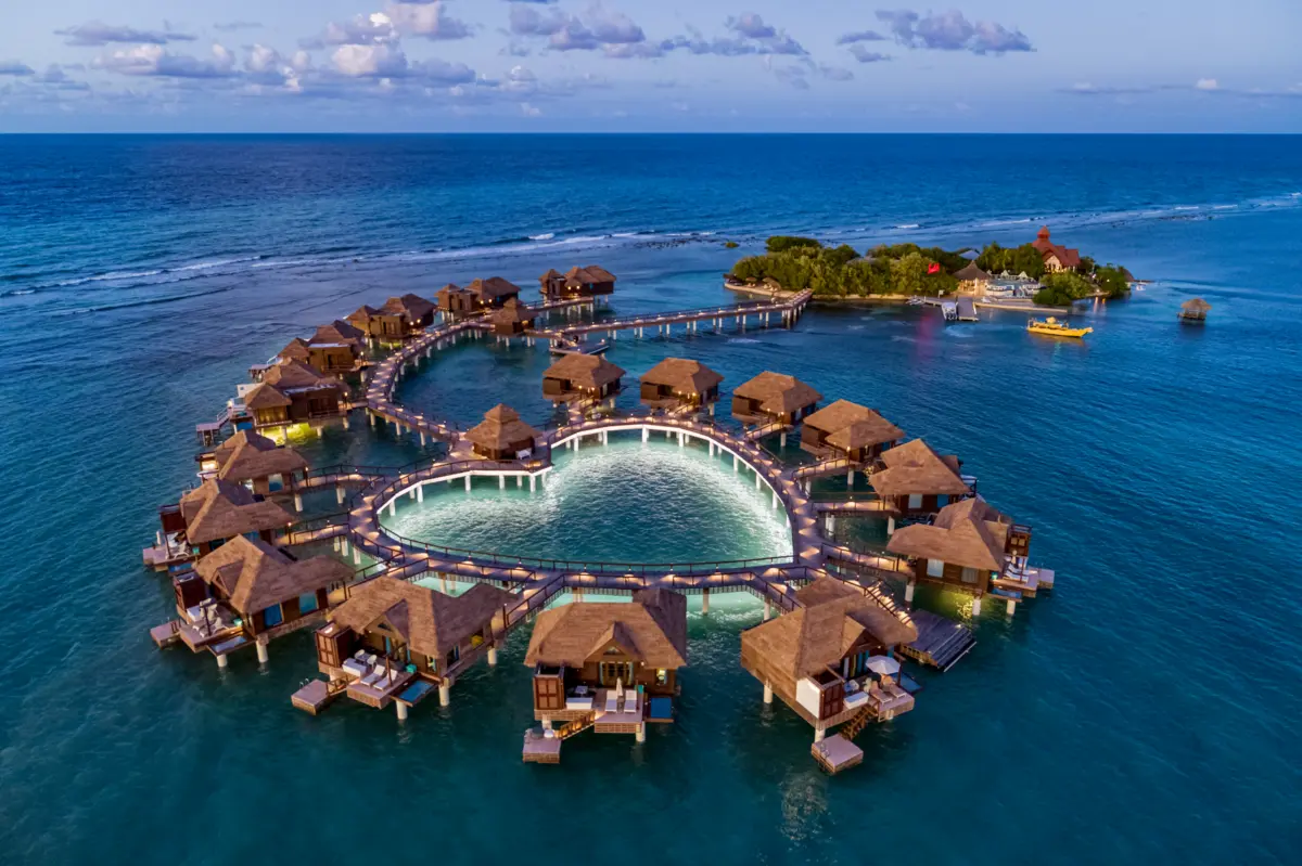 Overwater bungalows and illuminated walkways surrounding a pool at dusk.