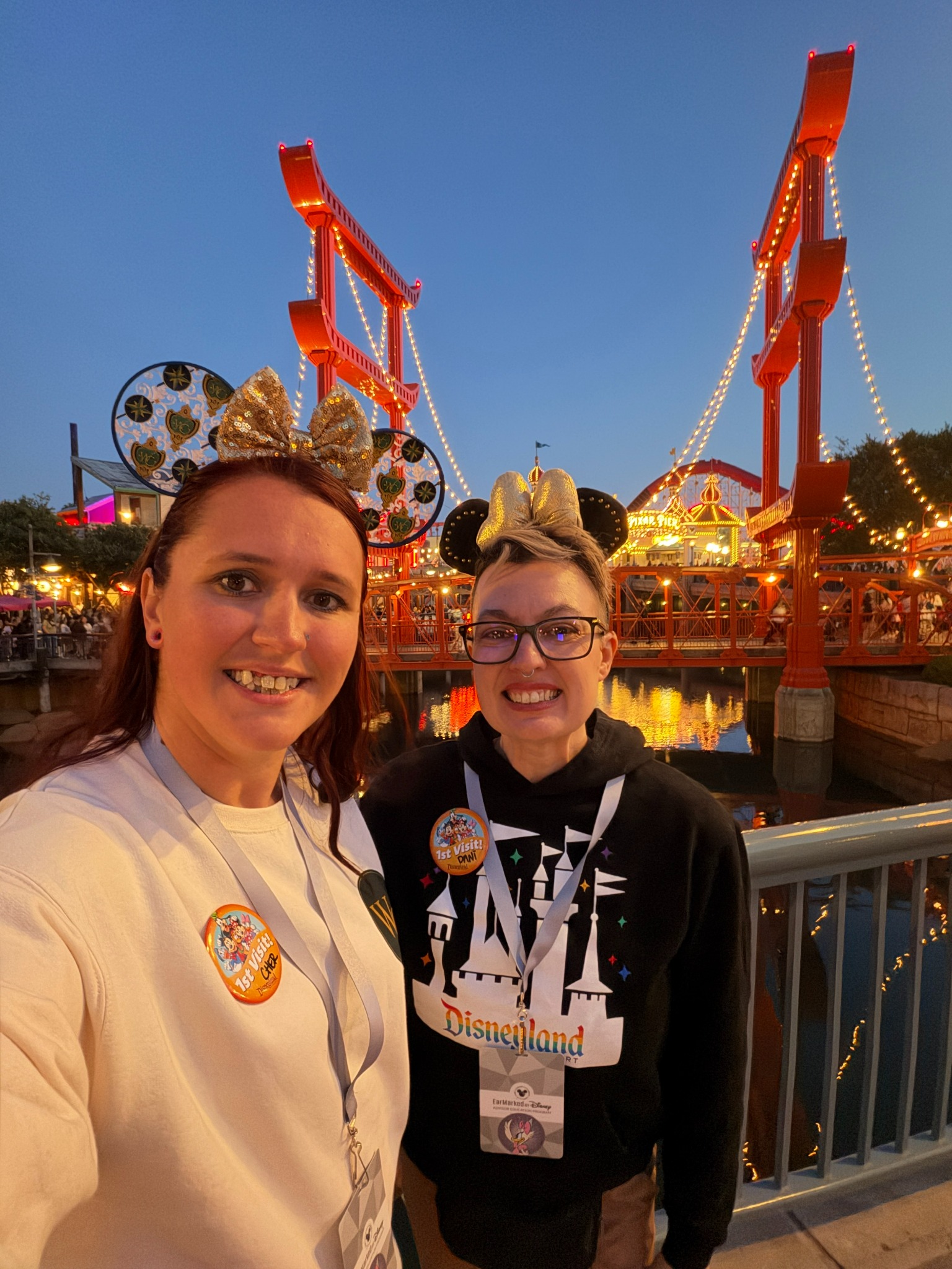 Two Wand & Compass advisors wearing Disney ears beside the illuminated bridge at Disney California Adventure.